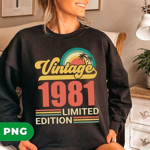 Pode incluir: Camisola preta de gola redonda com design retro. O gráfico apresenta o texto "Vintage 1981 Limited Edition" com um arco-íris, palmeiras e um design de pôr do sol. A camisola é de estilo vintage.
