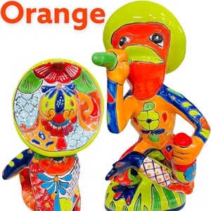 May include: Two colorful ceramic figurines of frogs wearing sombreros. The frog on the left is standing and holding a guitar. The frog on the right is sitting and holding a maraca. Both frogs are decorated with bright colors and intricate patterns.