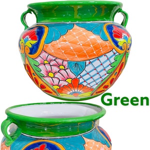 May include: A green glazed ceramic planter with two handles. The planter is decorated with colorful floral and geometric patterns in shades of orange, blue, green, yellow, red, and pink. The planter is a traditional Mexican Talavera style.