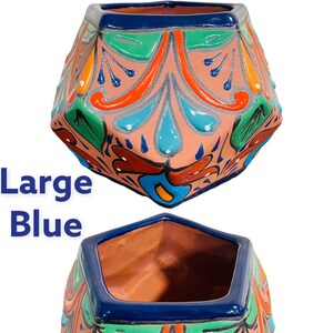 May include: A large, blue, hand-painted ceramic planter with a geometric shape and intricate floral designs. The planter has a light pink base with blue, green, orange, and red accents.