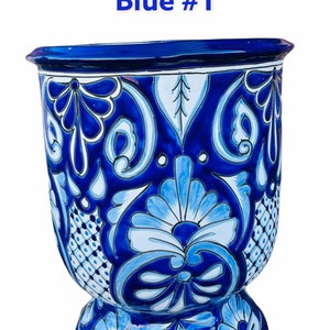 May include: Blue and white ceramic planter with a floral design. The planter has a wide base and a narrow top. The design is intricate and includes flowers, leaves, and geometric patterns.
