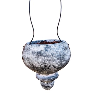 May include: A hanging planter made of gray ceramic with a distressed finish. The planter has a round body and a bulbous bottom. The planter is hanging from a black metal hook.
