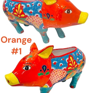 May include: Orange ceramic pig planter with colorful floral designs. The pig is standing on all four legs and has a yellow snout and ears. The planter has a large opening at the top for planting.