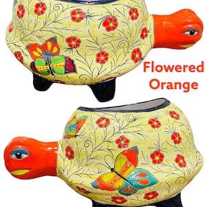 May include: A ceramic turtle planter with a yellow base, orange head and legs, and blue accents. The planter is decorated with red flowers, green leaves, and colorful butterflies. The text "Flowered Orange" is visible in the image.
