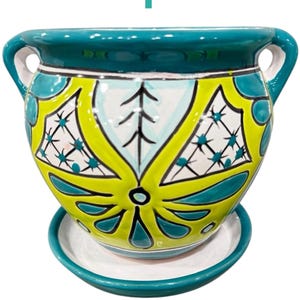 May include: Aqua ceramic planter with a green, yellow, and white geometric design. The planter has two handles and a matching saucer.