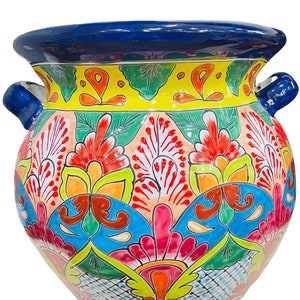 May include: A colorful Talavera pottery planter with a blue rim and intricate floral designs in shades of red, orange, yellow, green, and blue. The planter has two handles on the sides.