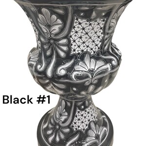 May include: Black and white ceramic vase with a floral design. The vase has a wide mouth and a round base. The vase is decorated with a white floral pattern on a black background. The vase is labeled "Black #1".