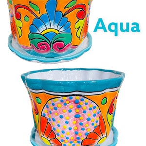 May include: A colorful ceramic planter with a turquoise rim and a bright orange background. The planter features a floral design with pink, yellow, blue, and green accents. The planter has a matching saucer.