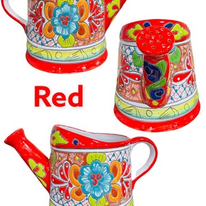 May include: Red ceramic watering can with a floral design. The can has a spout and a handle. The design features colorful flowers and leaves.