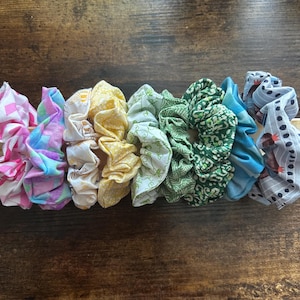 Peut inclure: Un ensemble de huit chouchous en tissu colorés avec différents motifs. Les chouchous sont disposés en rangée sur une surface en bois.