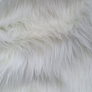 May include: White faux fur fabric with a soft, fluffy texture. The fur is arranged in a wavy pattern, creating a luxurious and cosy look.