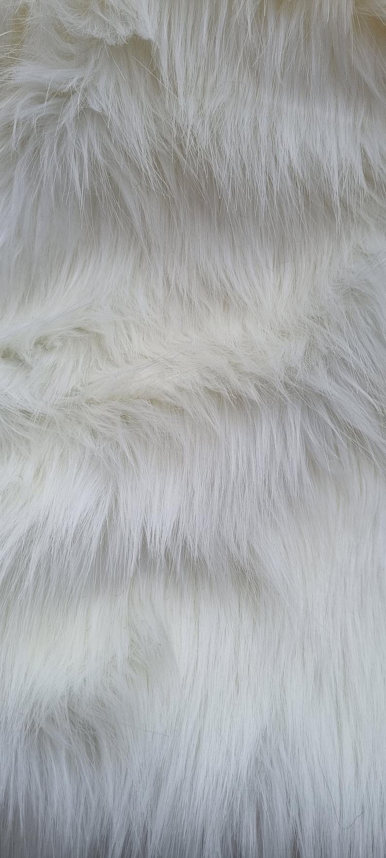 May include: White faux fur fabric with a soft, fluffy texture. The fur is arranged in a wavy pattern, creating a luxurious and cosy look.