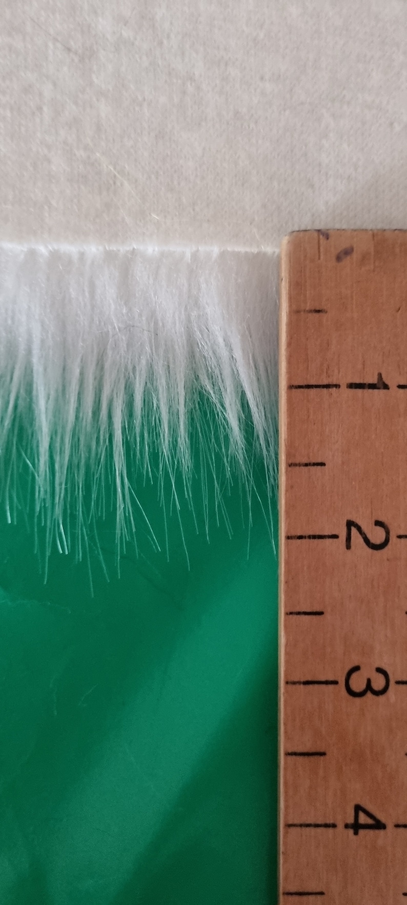 May include: White faux fur trim measuring approximately 7.6 cm in length. The fur is soft and fluffy, and it is shown against a green background.