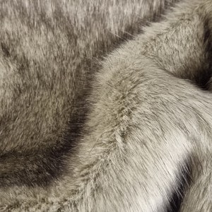 May include: Close-up of a soft, grey and white faux fur fabric. The fur is fluffy and has a subtle sheen.