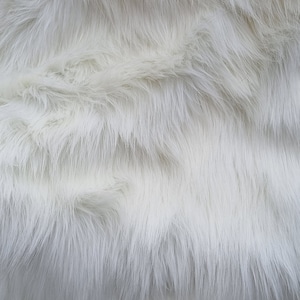 May include: White faux fur fabric with a soft, fluffy texture. The fur is arranged in a wavy pattern, creating a luxurious and cosy look.