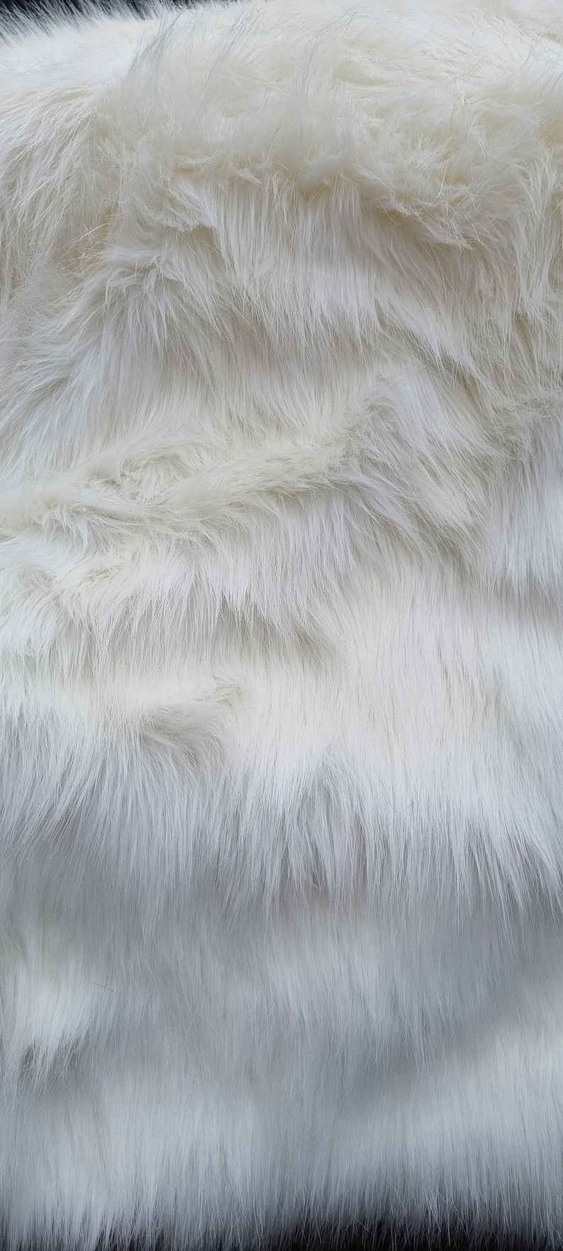 May include: White faux fur fabric with a soft, fluffy texture. The fur is arranged in a wavy pattern, creating a luxurious and cosy look.