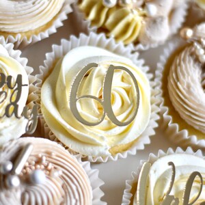 May include: Close-up of cupcakes decorated with white and beige frosting. One cupcake has a gold '60' topper.