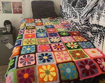 Könnte beinhalten: Eine bunte gehäkelte Decke mit einem Blumenmuster in den Farben Rosa, Grün, Blau, Gelb und Rot. Die Decke besteht aus Quadraten mit verschiedenen Blumendesigns.