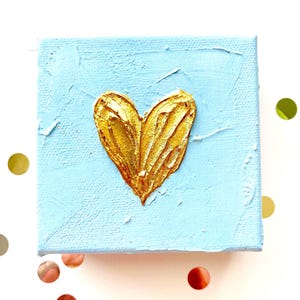 May include: A small, blue canvas painting with a gold heart painted in the center.