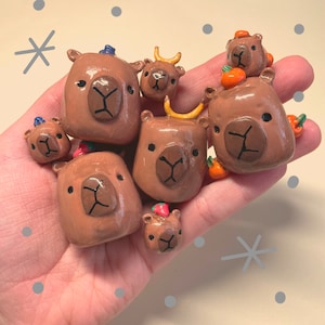 May include: A collection of nine small, hand-crafted ceramic animal figurines. The figurines are brown and feature a variety of animal faces, including bears, deer, and llamas. Each figurine has a small, orange, clay pumpkin on top of its head.