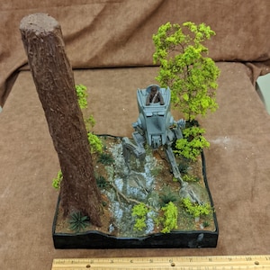 May include: A model of a Star Wars AT-ST walker with a Chewbacca figure in the cockpit. The walker is on a diorama base with trees and rocks.