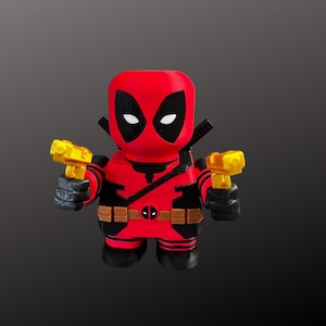 K&ouml;nnte beinhalten: Eine rot-schwarze Deadpool-Figur mit stilisiertem Design. Die Figur h&auml;lt zwei gelbe Spielzeugpistolen. Sie hat einen schwarzen G&uuml;rtel mit Deadpool-Logo und schwarze Handschuhe. Die Figur hat ein schwarz-rotes Farbschema.