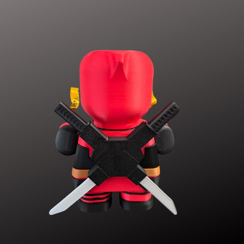 K&ouml;nnte beinhalten: Eine rot-schwarze Figur eines Superhelden, von hinten gesehen. Die Figur hat zwei gekreuzte Schwerter auf dem R&uuml;cken und gelbe Akzente. Die Figur tr&auml;gt einen schwarz-roten Anzug.