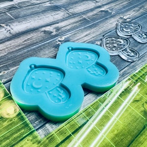 May include: Blue silicone mold with two mushroom-shaped cavities. Each cavity features a crescent moon and stars.