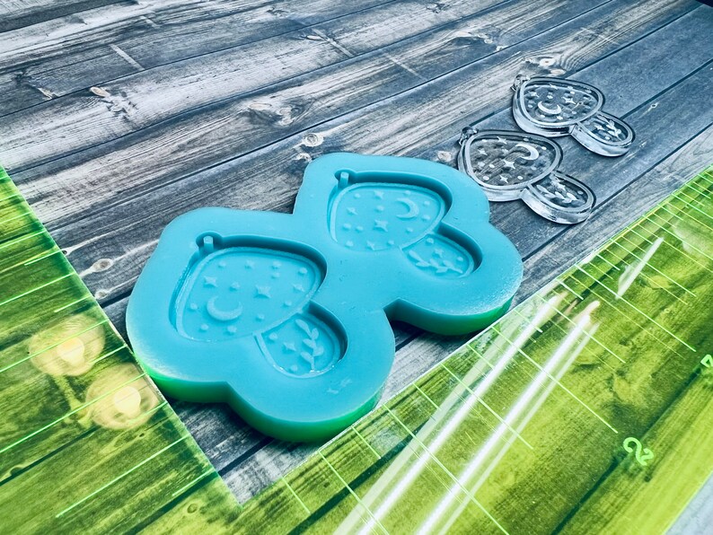 May include: Blue silicone mold with two mushroom-shaped cavities. Each cavity features a crescent moon and stars.