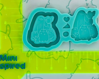May include: A teal blue silicone mold with a design of a ghost, a bird, and four cats. The mold is on a yellow ruler with the words "Mini Inspired" printed on it.