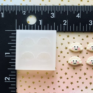 May include: A clear silicone mold with four impressions of a white dumpling with a smiling face. Four white dumplings with smiling faces are shown next to the mold.