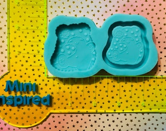 May include: Two blue silicone molds for making resin crafts. Each mold features a cartoon bear with a polka dot pattern and a flower on its head.