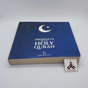 Könnte beinhalten: Ein blaues Buch mit einem Halbmond und einem Stern auf dem Cover. Der Titel lautet "Propheten im Heiligen Koran" mit den Worten "Touch & Feel" darunter. Das Buch liegt auf einer weißen Oberfläche mit einem kleinen Aufkleber, auf dem "Oudh Mania" steht.