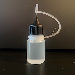 May include: A clear plastic bottle with a black screw-on cap and a thin, clear plastic dropper attached to the top.