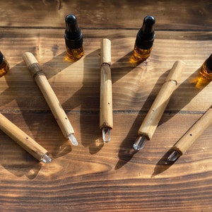 May include: Six wooden wands with clear crystal points and six small amber glass bottles with black droppers on a wooden surface.