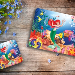 Op de afbeelding: Een kleurrijk placemat met Ariel, de Kleine Zeemeermin, die zwemt in een levendige onderwater scène met koraal, vissen en bubbels.