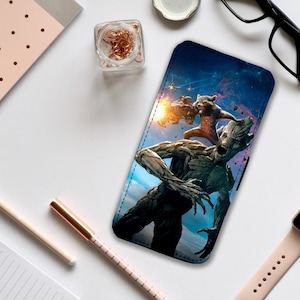 Puede incluir: Una funda para teléfono con una imagen colorida de dos personajes de la película Guardianes de la Galaxie. Los personajes son Rocket Raccoon y Groot. Rocket sostiene un arma y Groot está de pie detrás de él. El fondo es una galaxia con estrellas y planetas.