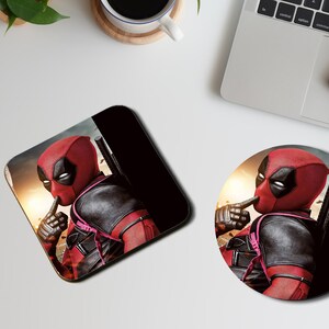 May include: A round and a square coaster featuring a superhero character with a red and black suit, a black mask, and a finger over his mouth. The background is a blurry image of a city skyline.