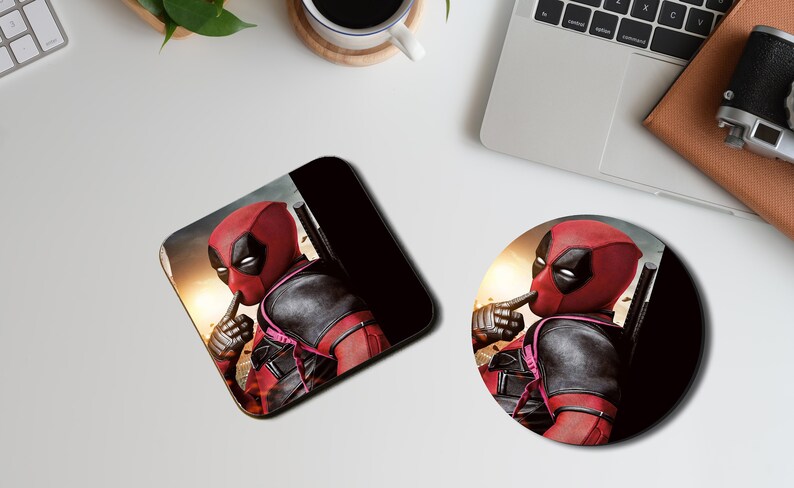 May include: A round and a square coaster featuring a superhero character with a red and black suit, a black mask, and a finger over his mouth. The background is a blurry image of a city skyline.