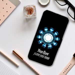 Może przedstawiać: Czarne etui na telefon z niebieskim i srebrnym wzorem Iron Mana. Etui ma nadrukowany tekst "Your Name I Love You 3000".