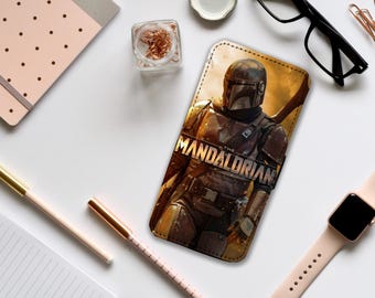 Può includere: Una custodia per telefono in pelle marrone con una grafica di un personaggio mandaloriano della serie Star Wars. Il testo "The Mandalorian" è stampato sulla custodia.
