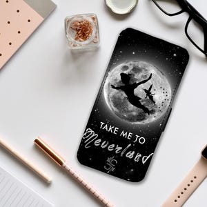 Puede incluir: Carcasa de teléfono negra con una silueta de Peter Pan volando con Campanilla frente a una luna llena. El texto "Take Me To Neverland" está escrito debajo de la luna.