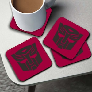 Può includere: Set di quattro sottobicchieri quadrati rossi con un logo Transformers nero. I sottobicchieri sono realizzati in un materiale simile al sughero.