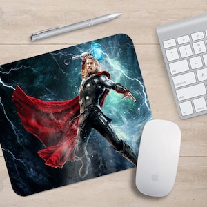 May include: A mouse pad featuring a superhero character with a red cape and a hammer. The character is standing in front of a blue and green background with lightning bolts.