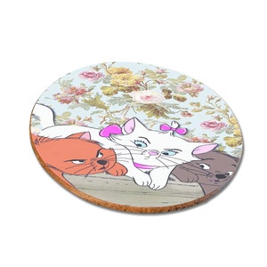 May include: A round coaster with a floral pattern featuring three cartoon cats. The white cat is in the center with a pink bow and the orange and gray cats are on either side.