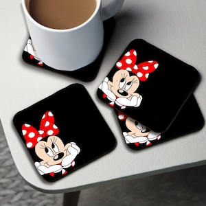 May include: Set of four black square coasters featuring a cartoon image of Minnie Mouse with red polka dot bow. The coasters are made of wood and are perfect for protecting surfaces from heat and spills.