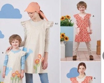 May include: A sewing pattern for a child's dress with a floral print and a matching apron. The pattern is called "Simplicity" and the number is S9767. The pattern is easy to sew and includes instructions for making a hat.