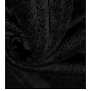 May include: Close-up of a black, plush fabric with a soft, textured surface. The material appears to be thick and luxurious, with visible fibers creating a rich, dark appearance. The fabric is folded, creating shadows and depth.