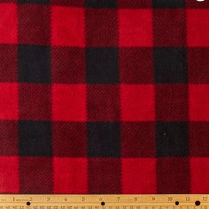 May include: A close-up of a red and black buffalo plaid fabric. The fabric has a repeating pattern of large, evenly sized squares in a classic check design. The fabric is soft and textured.