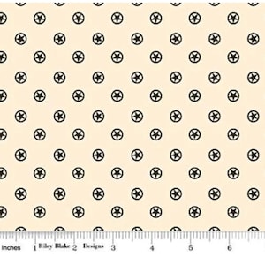 May include: Cream-colored fabric with a repeating pattern of black stars inside circles. The stars are evenly spaced across the fabric. A ruler with inch measurements is at the bottom. The text "Riley Blake Designs" is also visible.